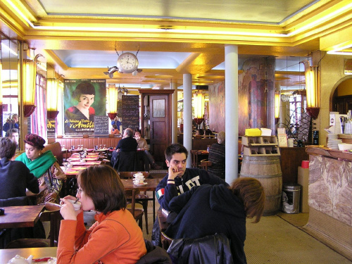 W Les Doux Moulins, kawiarni, gdzie filmowa Amelia pracowała jako kelnerka, panuje ciągły ruch. Z olbrzymiego plakatu w głębi, na delektujących się filiżanką kawy, spogląda Audrey Tautou. #Paryż #Francja